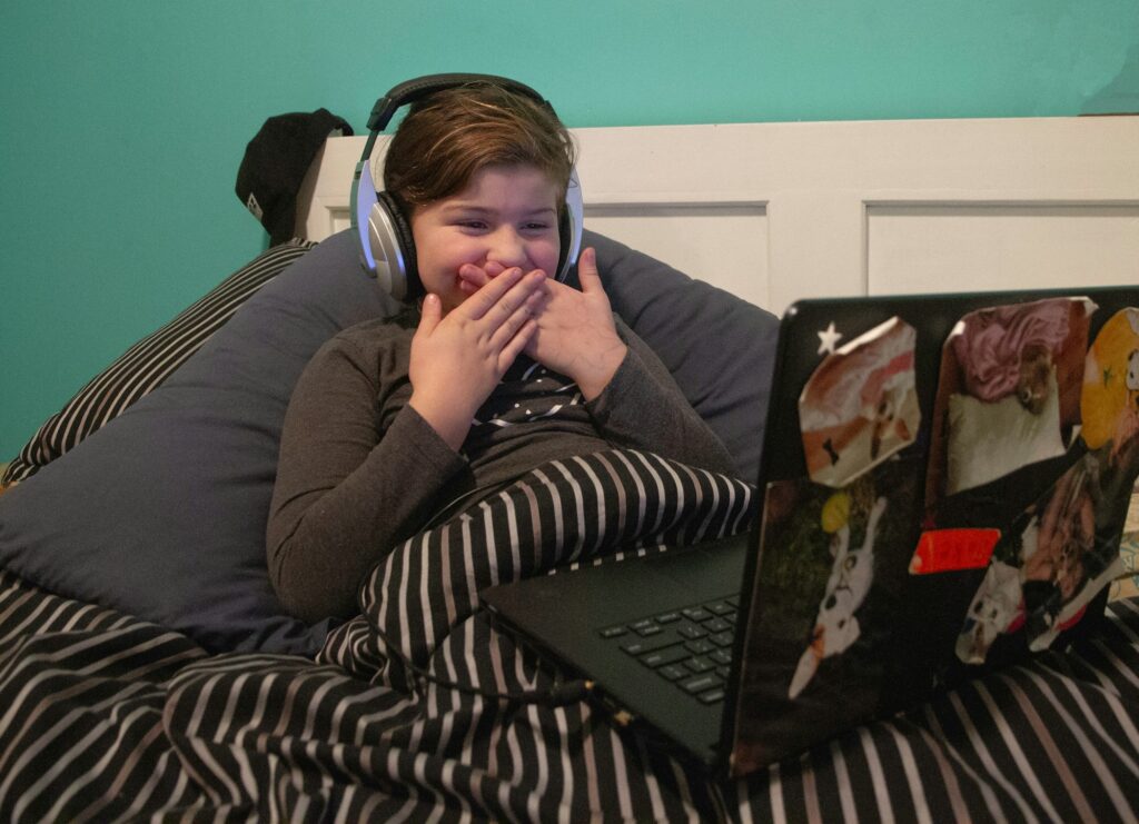 child in bed on laptop/ computer with smile on face, watching her favourite TV Show.