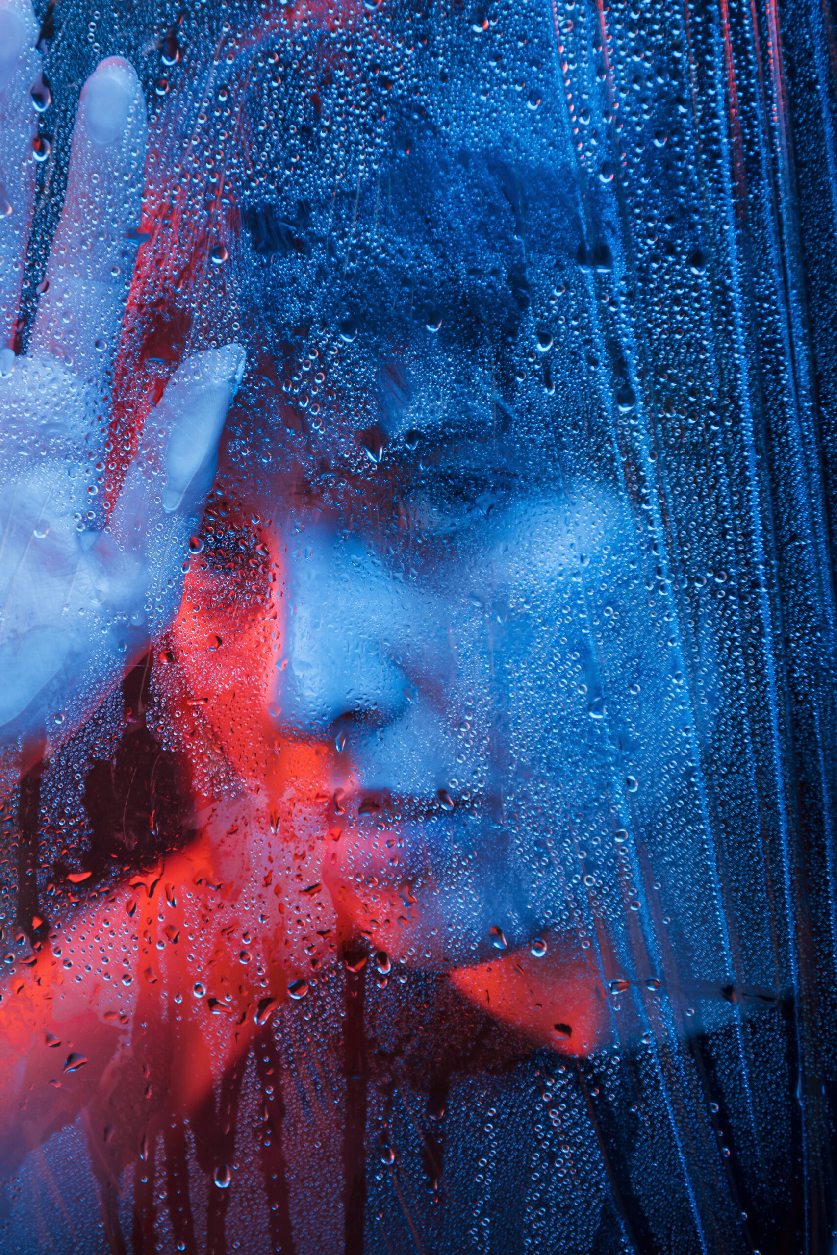 Gorgeous woman. Studio shot in dark studio with neon light. Portrait of beautiful girl behind wet glass.